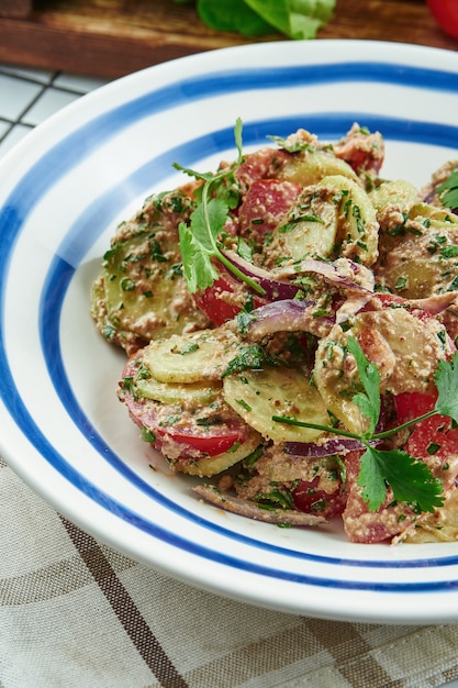 Photo salade géorgienne de légumes avec tomates, concombre et oignons assaisonnés de sauce aux noix dans un bol blanc. salade dans une composition avec des ingrédients. fermer.