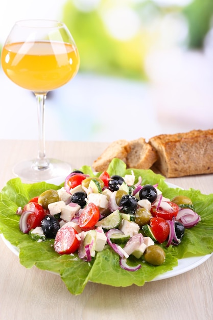 Salade grecque en assiette et verre de vin sur table en bois sur fond naturel