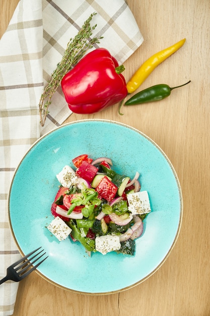 Salade grecque aux olives, tomates, fromage feta, oignons dans un bol bleu sur mur en bois. Fermer. Mise au point sélective
