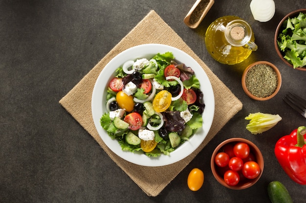 Salade grecque fraîche en assiette et ingrédients sur table en pierre