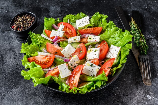 Salade grecque fraîche avec légumes et fromage feta dans une assiette. Table noire. Vue de dessus.