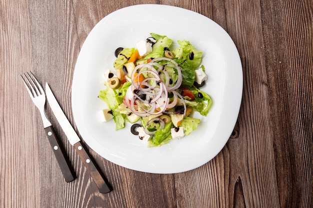 Salade grecque avec légumes frais tomate concombre poivron rouge laitue oignon olives et fromage Gros plan sur une plaque ronde blanche sur un fond en bois