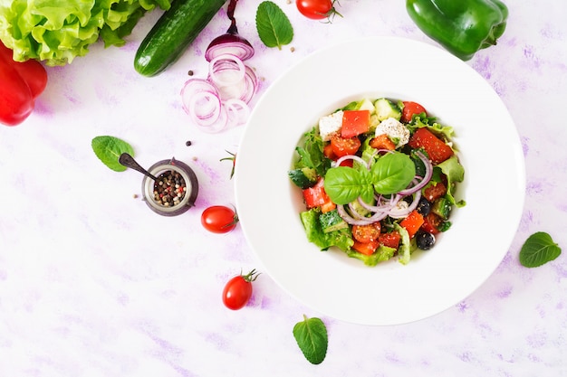 Salade grecque avec tomate fraîche, concombre, oignon rouge, basilic, laitue, fromage feta, olives noires et herbes italiennes. Vue de dessus