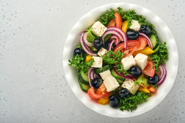 Salade grecque traditionnelle de concombre frais, tomate, poivron, laitue, oignon rouge, fromage feta et olives à l'huile d'olive sur plaque blanche. Alimentation saine, vue de dessus.