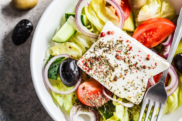 Salade grecque traditionnelle avec feta, olives, tomates et concombre dans un plat blanc, vue de dessus.