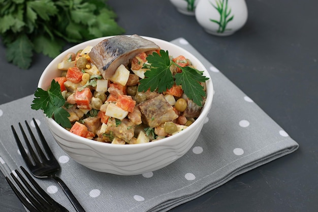 Salade de hareng aux œufs de carottes et aux pois dans un bol blanc sur fond gris foncé