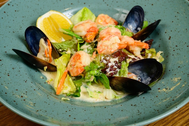 Photo salade d'huîtres, crevettes et légumes sur plaque bleue sur fond de bois, vue du dessus