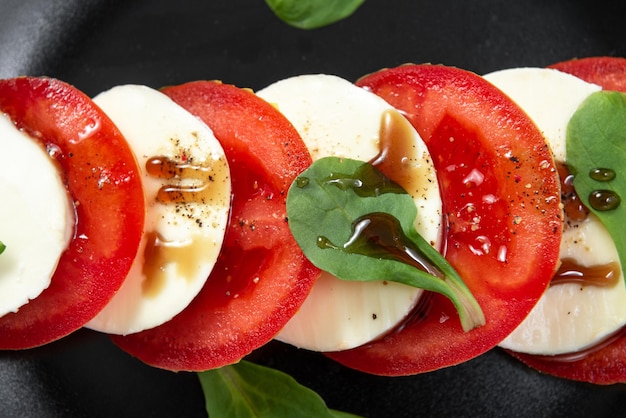 Salade italienne sur une plaque noire avec du fromage et des tomates Salade caprese de cuisine européenne avec des tomates à l'huile d'olive et du fromage mozzarella et du poivre noir