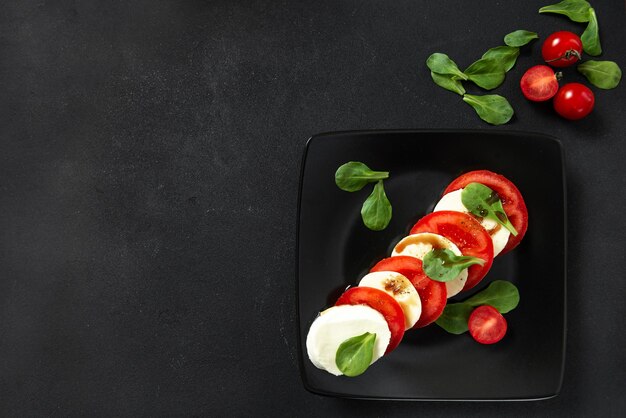 Salade italienne sur une plaque noire avec du fromage et des tomates Salade caprese de cuisine européenne avec des tomates à l'huile d'olive et du fromage mozzarella et du poivre noir