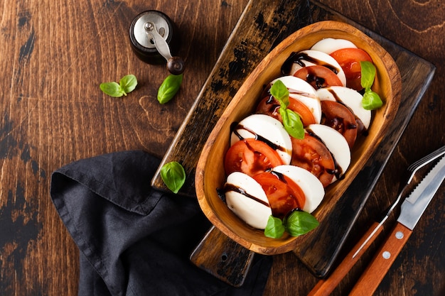 Salade italienne traditionnelle caprese dans un bol en bois d'olive sur fond rustique ancien