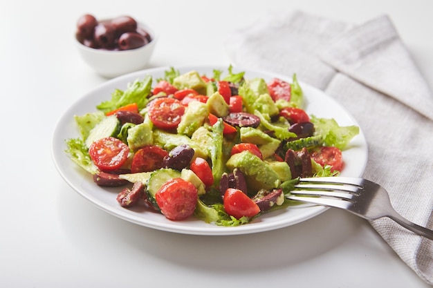 Salade de laitue concombres tomates olives et avocats en plaque blanche sur la table