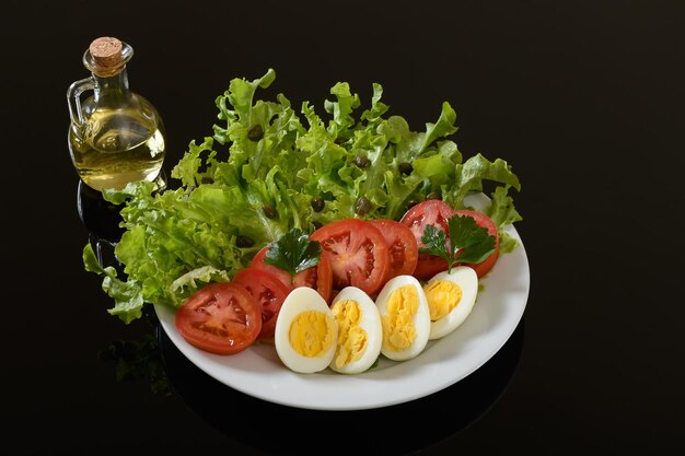 Salade de laitue, tomate, oeuf et câpres sur une assiette blanche sur fond noir
