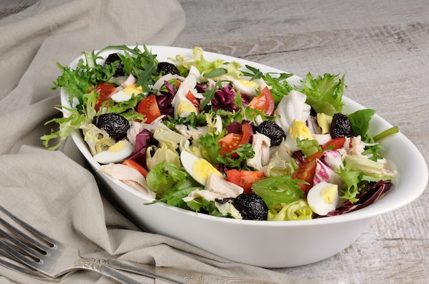 Salade légère du mélange de feuilles de laitue avec tomates, œufs, tranches de poitrine de poulet et olives séchées