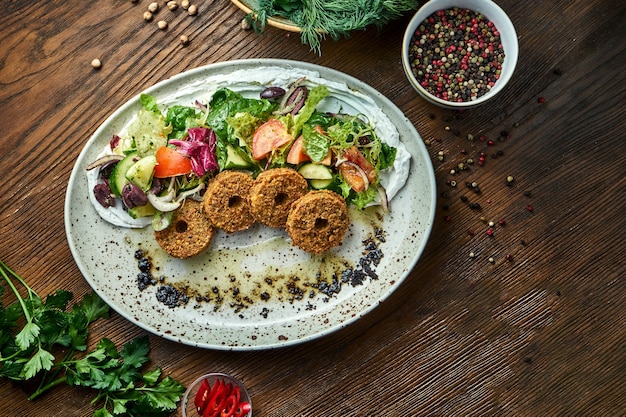 Salade de légumes aux falafels et huile d'olive servie dans une assiette bleue sur un fond en bois. Nourriture de restaurant