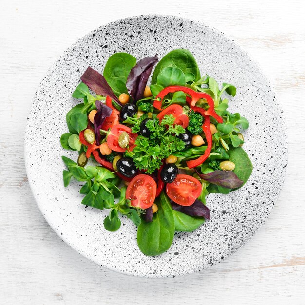 Salade de légumes aux tomates épinards paprika et graines de citrouille dans une assiette sur un fond en bois Vue de dessus Espace libre pour votre texte Mise à plat