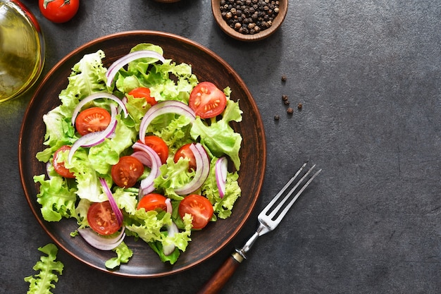 Salade de légumes aux tomates, oignons rouges et sauce sur fond noir, vue du dessus