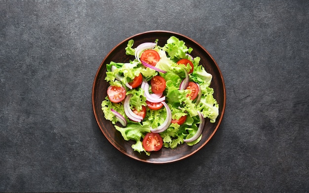 Salade de légumes aux tomates, oignons rouges et sauce sur fond noir, vue du dessus