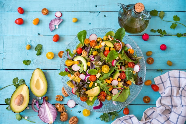 salade de légumes biologiques frais et une bouteille d'huile d'olive extra vierge sur fond bleu