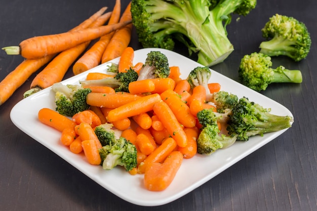 Salade de légumes: brocoli et carottes dans une assiette blanche sur fond noir