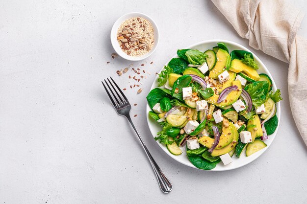 Salade de légumes avec concombre d'avocat et feta assaisonnée de noix et de graines sur fond gris Vue de dessus copie espace