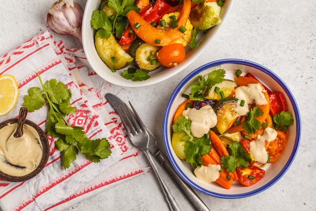 Salade de légumes cuits au four avec tahini en plaque blanche, fond blanc, vue de dessus. Concept de restauration propre.