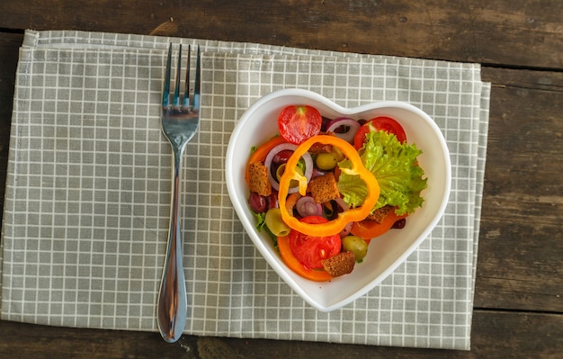Salade de légumes dans une assiette en forme de coeur sur une table en bois sur une serviette.