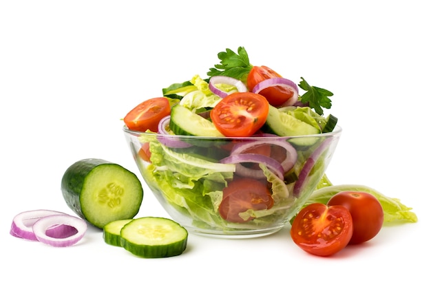 Salade de légumes dans une assiette en verre et ingrédients concombre, tomates, oignon sur un blanc isolé.