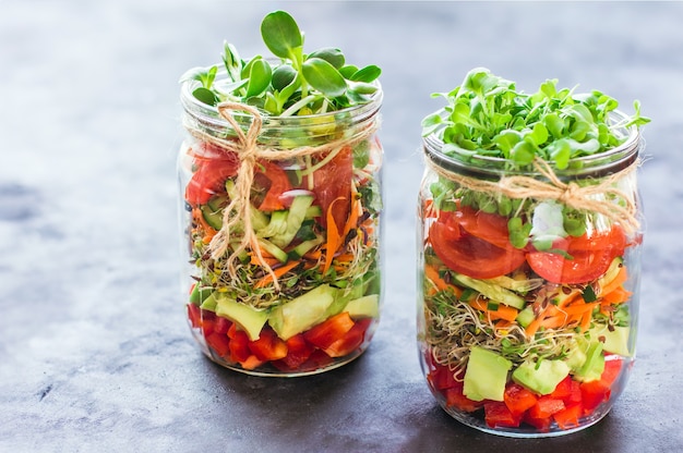 Salade de légumes dans des bocaux ouverts sur fond de marbre clair