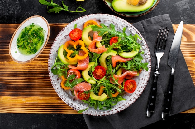 Salade de légumes d'été frais avec roquette, tomates, poivrons, avocat et saumon sur une assiette vue de dessus.