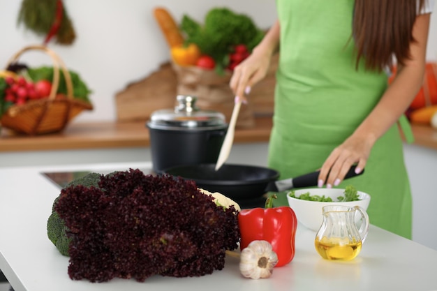 Salade de légumes frais et huile végétale à l'arrière-plan de la femme cuisine près de la cuisinière dans la cuisine