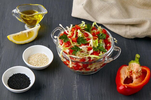 Salade de légumes frais et légers de chou haché et de poivrons doux, habillée de citron et d'huile d'olive, entourée d'ingrédients sur une table en béton noir