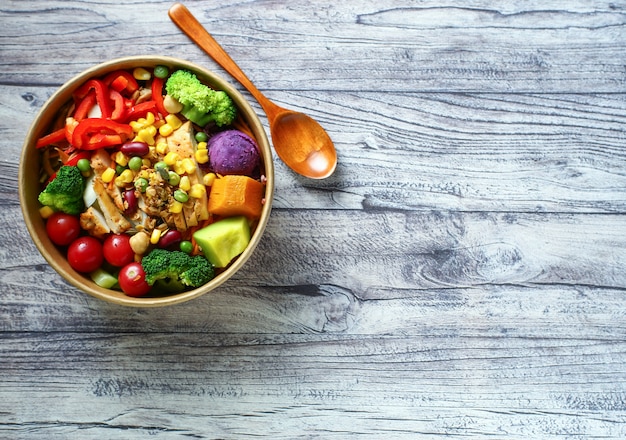 salade de légumes et poulet dans un bol en papier sur une table en bois