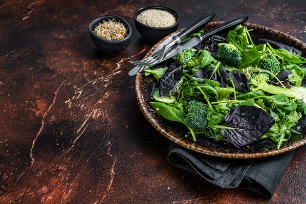 Salade de légumes sains avec des feuilles fraîches de roquette, laitue, épinards pour salade végétalienne. Fond sombre. Vue de dessus. Copiez l'espace.