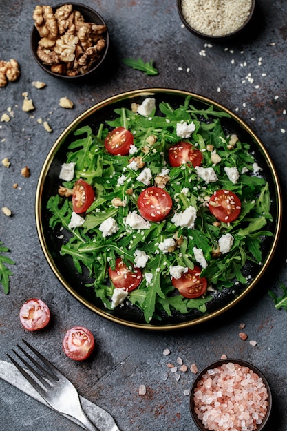 Salade de légumes sains avec roquette fraîche, tomate, fromage feta et noix sur une plaque sombre. Menu diététique