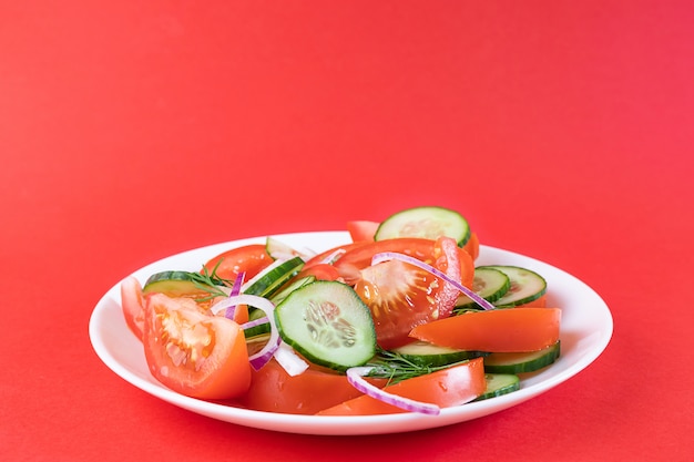 Salade de légumes simple de tomate, concombre, oignon et aneth en plaque blanche sur fond rouge vif.