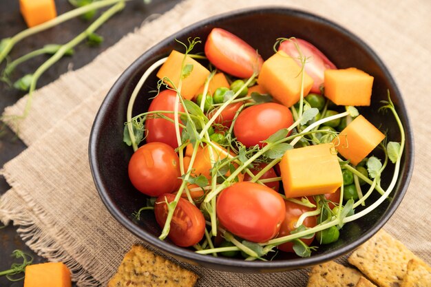 Salade de légumes végétarienne de tomates, potiron, pousses de pois microgreen sur béton noir