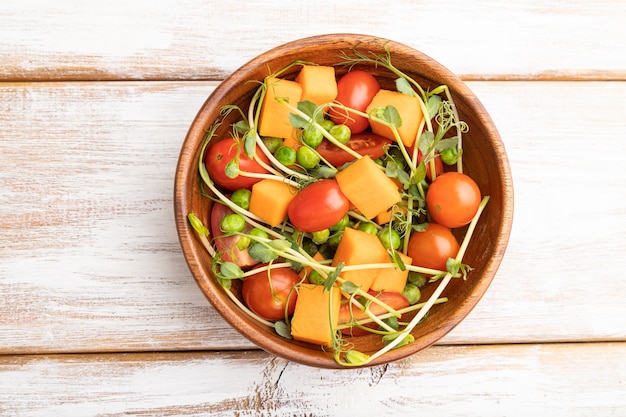 Salade de légumes végétariens de tomates, citrouille, pousses de pois microgreen sur bois blanc