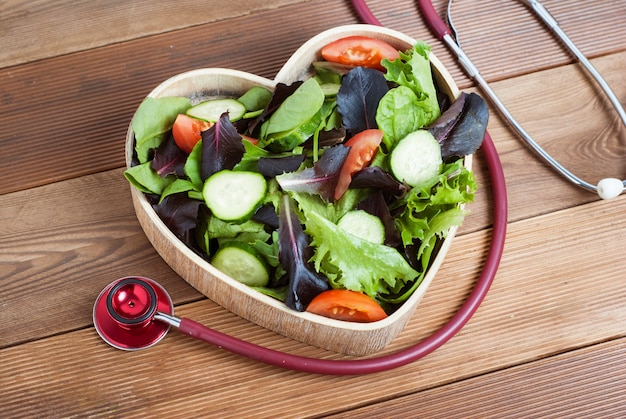 Salade de légumes verts en plaque de bois et stéthoscope en forme de coeur.