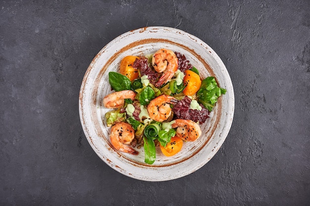 Salade maison aux crevettes frites, tomates jaunes, roquette, épinards, laitue et sauce sur un bol en céramique