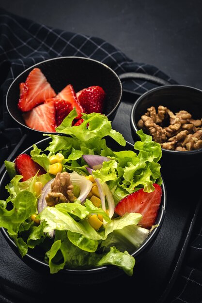 Salade maison avec laitue, fraises, oignon rouge, maïs; huile d'olive et noix dans un bol. Concept de nourriture végétalienne