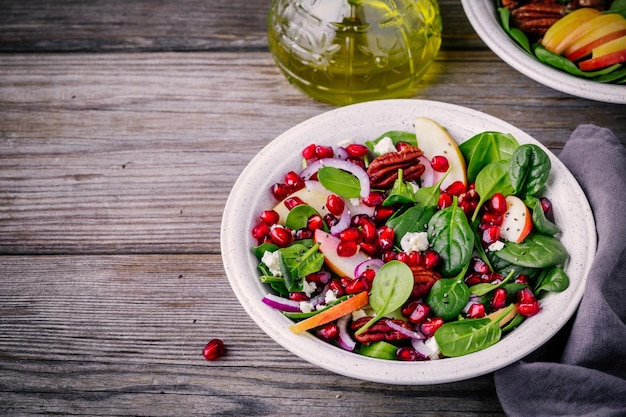 Salade maison d'oignon rouge de pécan de pomme d'épinards avec le fromage de chèvre et la grenade sur le fond en bois