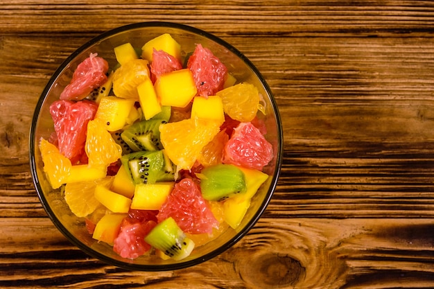 Salade de mangue, oranges, pamplemousses et kiwis dans un bol en verre sur une table en bois. Vue de dessus