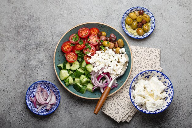 Salade méditerranéenne grecque avec tomates, fromage feta, concombre, olives entières et oignon rouge dans une assiette en céramique bleue sur fond de béton gris d'en haut, apéritif traditionnel de la Grèce