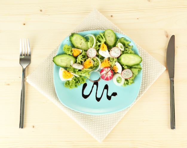 Salade mélangée fraîche avec des oeufs, des feuilles de salade et d'autres légumes sur le plat de couleur, sur la table en bois