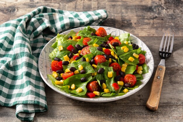 Salade mexicaine avec haricots noirs, maïs, tomates, laitue et poivre sur table en bois