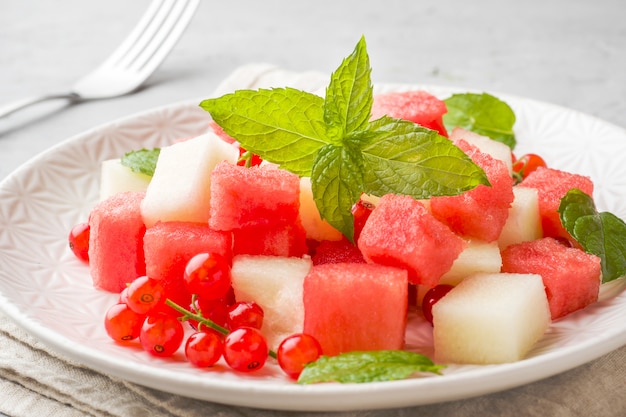 Salade de morceaux juteux frais de melon d'eau, melon, groseille et menthe feuilles sur une assiette.