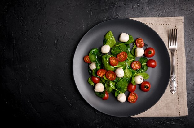 Salade de mozzarella et jeunes épinards sur plaque en céramique noire.