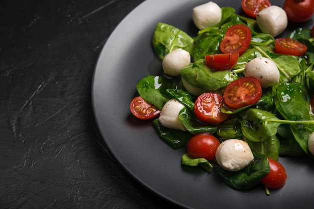 Salade de mozzarella et jeunes épinards sur plaque en céramique noire.