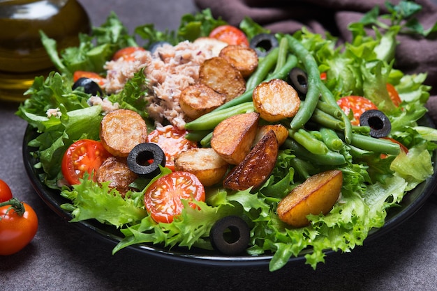 Salade niçoise au thon, tomates, pommes de terre et haricots verts sur fond sombre, gros plan