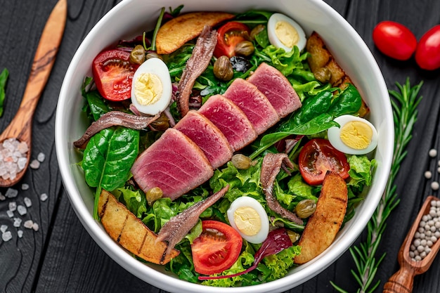 Photo salade nisuaz avec du thon, des anchois, des pommes de terre, des tomates cerises, du mélange d'huile d'olive et d'œufs de caille cuisine française